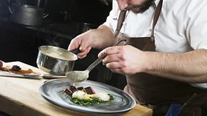 Kock lägger upp mat på tallrik.