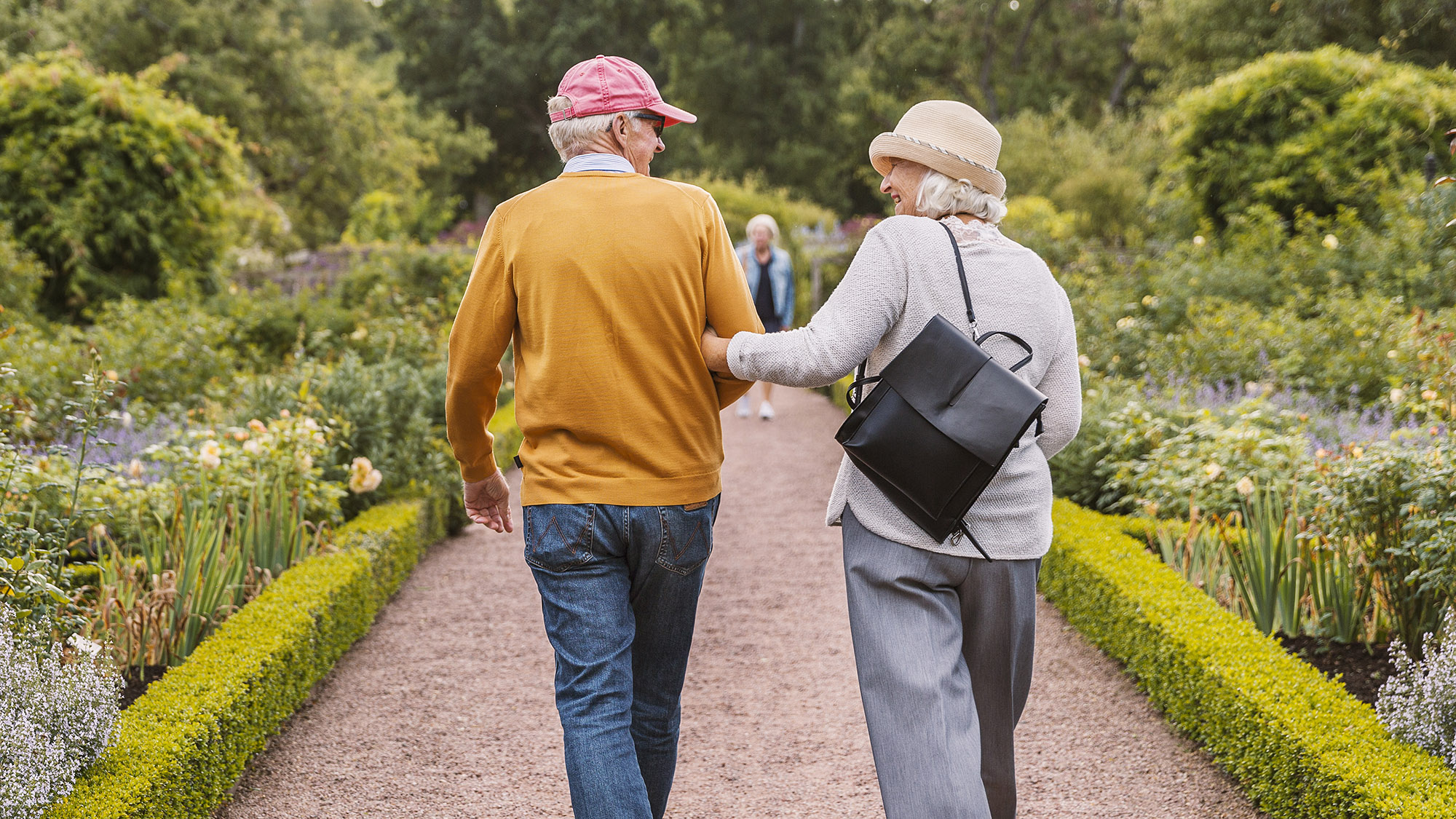 Äldre par som promenerar i trädgård.